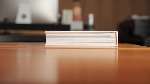 Hand placing heavy white book on wooden table in a design studio. Tight shot from table top.