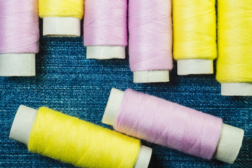 Spools of pink and yellow sewing thread on blue denim
