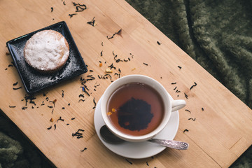 Homemade cupcake with powdered sugar on a black plate and a white cup of tea with natural additives...