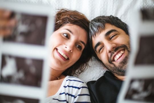 Happy pregnant couple on the bed looking at the ultrasound images of their baby