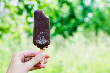 Chocolate ice cream in chocolate glaze on a stick in a female hand on a green background