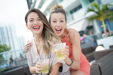 Two attractive funloving friends partying with drinks on rooftop bar in city