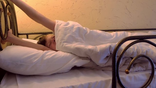 Boy sleeps at hostel on bunk bed wakes up, stretches and yawns.