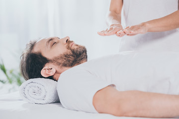 side view of bearded man with closed eyes receiving reiki treatment on chest