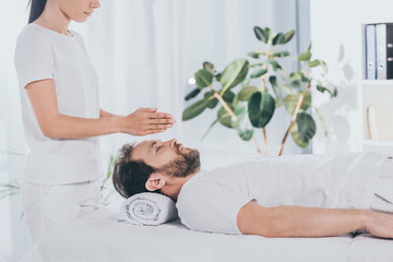 Obraz premium side view of calm bearded man with closed eyes receiving reiki treatment on massage table