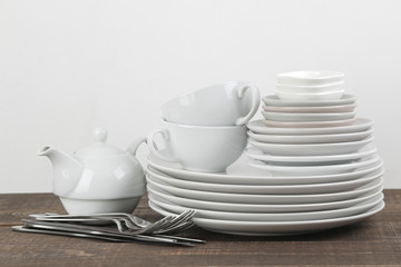 A stack of dishes. tableware on a brown wooden table. plates and cutlery, cups and kettle.