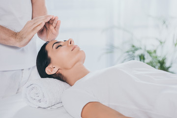 cropped shot of calm young woman with closed eyes receiving reiki therapy - obrazy, fototapety, plakaty