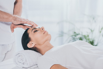 cropped shot of calm young woman with closed eyes receiving reiki treatment on head - obrazy, fototapety, plakaty