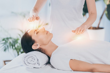 side view of calm young woman receiving reiki healing therapy on head and chest