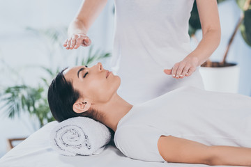 cropped shot of calm young woman receiving reiki healing therapy on head and chest - obrazy, fototapety, plakaty