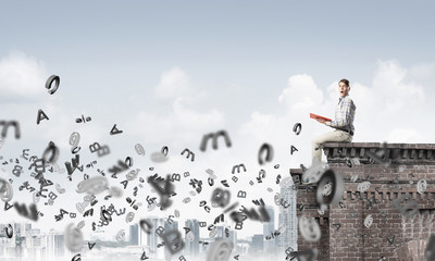 Man on roof edge reading book and symbols flying around