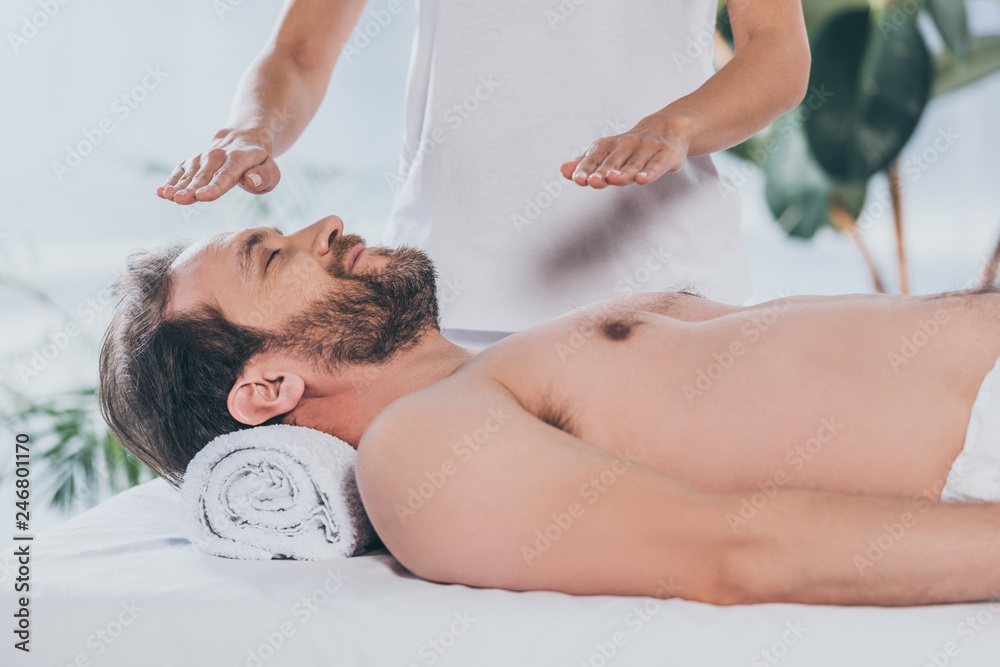 Wall mural calm bearded man with closed eyes lying and receiving reiki treatment - Wall murals
