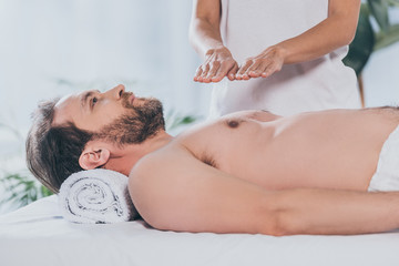 Obraz na płótnie Canvas cropped shot of peaceful bearded man receiving reiki treatment on bare chest