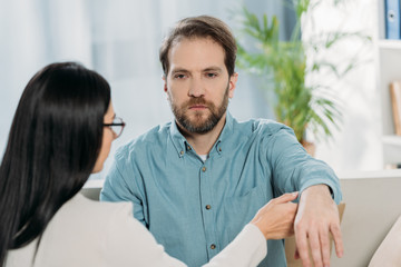 Fototapeta premium young woman in eyeglasses holding hand of bearded man during hypnotherapy