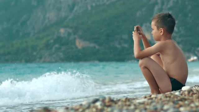 Child enjoying vacation at sea. Boy playing video games on mobile phone at beach