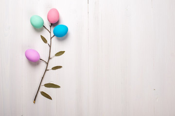 Spring twig with Easter painted eggs lies on a white wooden background.