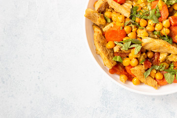 Curry with chickpea, turkey, carrot, leek and dried apricots in a white plate. Healthy food. Concrete background. Copy space.