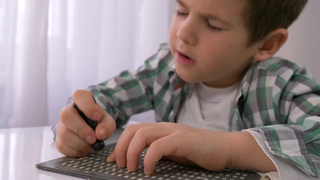education of blind children, sick little boy learning to write characters font Braille at table in bright indoor
