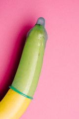 Close up of green condom on fresh yellow banana in front of pink background