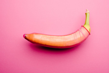 Pink condom on fresh banana in front of pink background