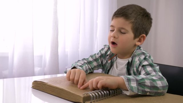 learning for blind, ill kid boy reading braille book with characters font for Visually impaired sitting at table indoors