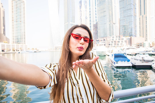 Young pretty woman tourist in sunglasses blow kiss taking selfie photo in Dubai Marina in United Arab Emirates.