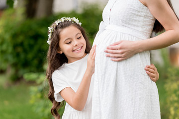 Fototapeta premium cropped shot of adorable happy child in floral wreath touching belly of pregnant mother in park
