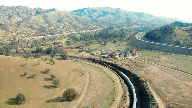 The aerial camera falls back from the four locomotives out front going to the western direction around the rail loop and continues rotating to the left and to the northern part of the rail loop.