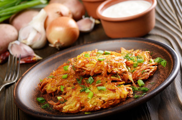 Fresh homemade tasty potato pancakes in clay dish with vegetables on wooden table