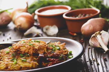 Homemade tasty potato pancakes in clay dish with sun-dried tomatoes and sour cream