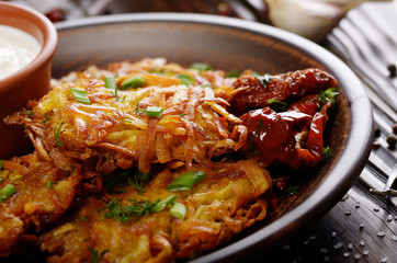 Closeup view at Homemade tasty potato pancakes in clay dish with sun-dried tomatoes and sour creram