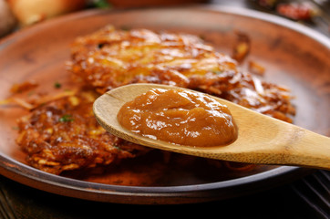 Applesauce in front of fresh homemade tasty potato pancakes in clay dish