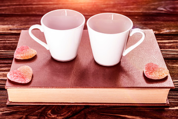 two cups of coffee, candy in the form of a heart on the book on the background of a wooden table. love, romantic date. Valentine's day.