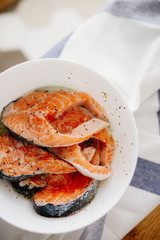 Portions of fresh salmon fillet with aromatic herbs and spices in a bowl on the table in the kitchen