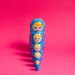 A row of five stacking Russian dolls, painted with a blue and pink pattern, against a bright pink background