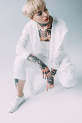 attractive woman with tattoos sitting on grey background