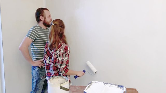 Handsome Father is Showing his Daughter how to Paint Walls. Happy Family - Man and Teen Girl doing Repairs at Home together. Dad and Child Painting Wall in flat in white, using a roller.