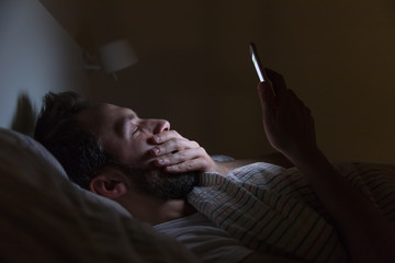 Adult sleepy yawning male awake late at night in bed surfing in web, can not fall asleep/ sleepy tired, social media addiction, dependency on cell phone, half-closed tired eyes, sleeplessness concept.