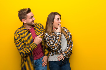 Couple in valentine day pointing finger to the side with a surprised face