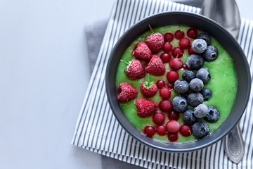 Breakfast kiwi smoothie bowl topped with frozen raspberry, blueberry and red currant on gray wooden background. Top view. Copy space
