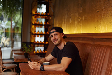 Cheerful young Caucasian man in sporty outfit blinks eye and has appealing smile, flirts with beautiful woman who stands before, tells jokes or funny stories, invited to sit beside at modern cafe .