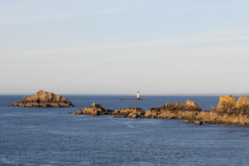 Fototapeta na wymiar rocks in the water and a white lighthouse at the coast in bretagne, france in summer