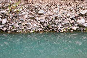 Stone shore of river and its reflection in turquoise water surface.