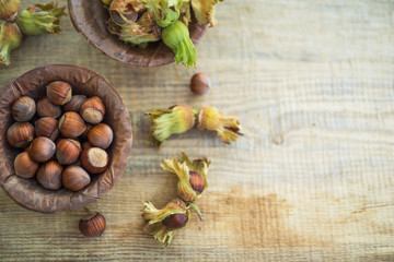 Flat lay photo composition of just harvested whole hazelnuts with shells in a plate of dried leaves on the rustic wooden board. Selective focus.
