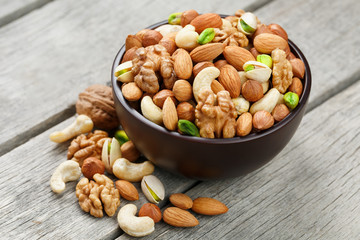 Wooden bowl with mixed nuts on a wooden gray background. Walnut, pistachios, almonds, hazelnuts and cashews, walnut.