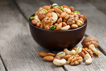 Naklejka na ściany i meble Wooden bowl with mixed nuts on a wooden gray background. Walnut, pistachios, almonds, hazelnuts and cashews, walnut.