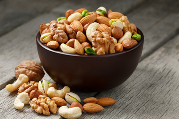 Wooden bowl with mixed nuts on a wooden gray background. Walnut, pistachios, almonds, hazelnuts and cashews, walnut.