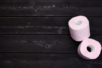 Pastel pink toilet paper rolls on black wooden background