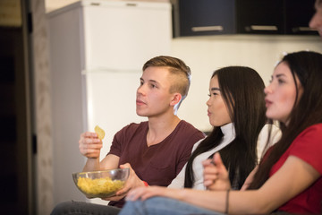 Company of young friends spending time together watching TV and eating popcorn and chips