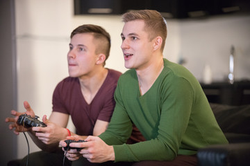 Company of young friends spending time together. Two young man playing game